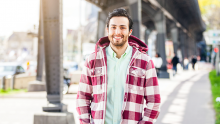 Smiling man in plaid jacket standing under a long bridge