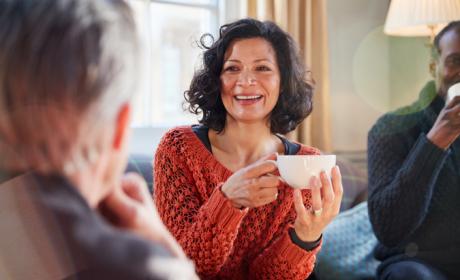 Woman in jumper smiling, holding a white cup and talking to people in a group