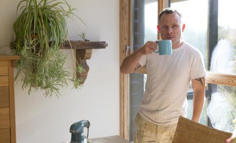 Man in white t-shirt standing, drinking from a blue mug