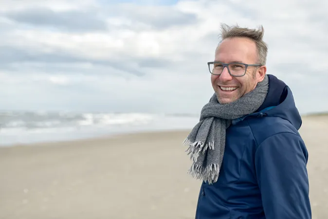 Man in blue jacket, wearing a scarf and standing on a beach