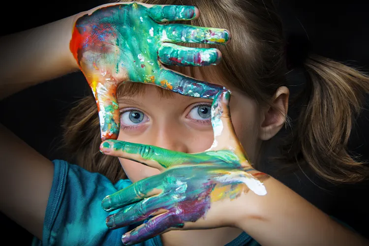 Child with messy paint hands looking through fingers