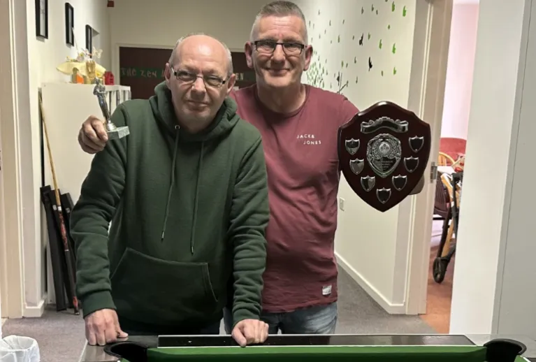 Two men holding up trophies at a pool table